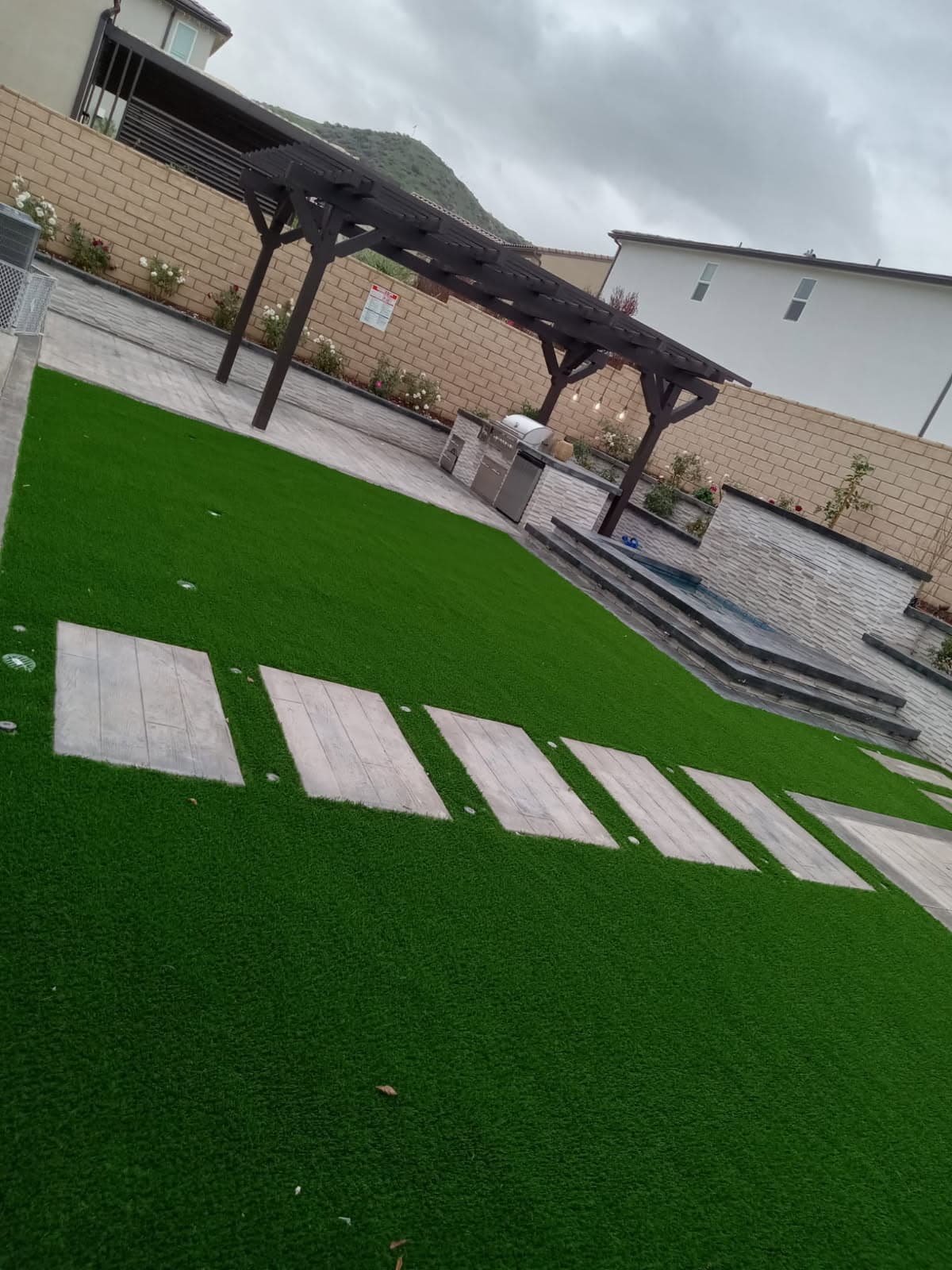 Artificial turf backyard with paver stepping stones and a pergola